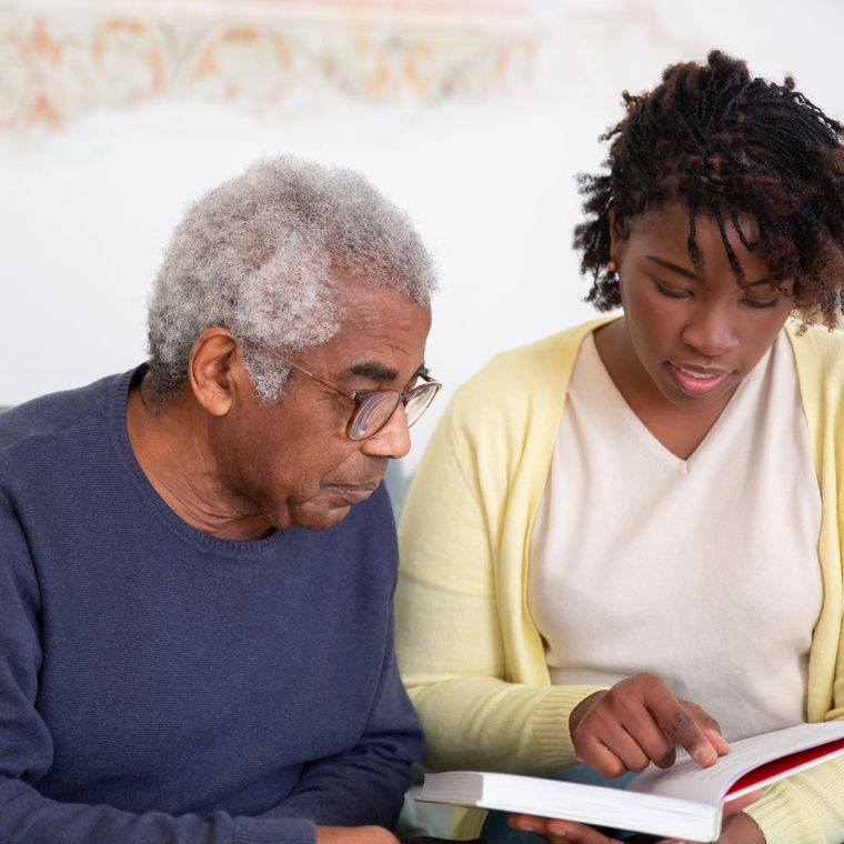 A caregiver reading a book with an older man at home